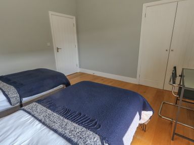 A bedroom with two beds covered in blue blankets and a chair next to a glass desk at Stapleford Farm in Hooke near Beaminster