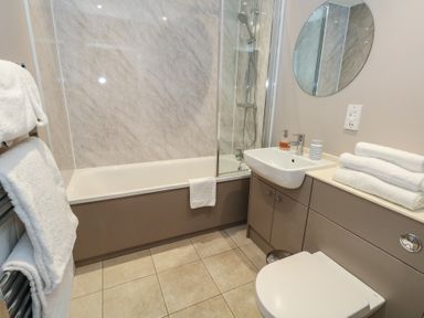 A bathroom with a bathtub shower combination a sink with a round mirror and a toilet at Stapleford Farm in Hooke near Beaminster