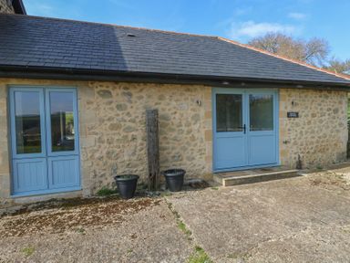 A stone building with blue double doors and two black plant pots outside at Stapleford Farm in Hooke near Beaminster