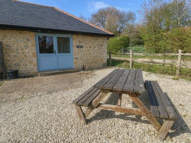 A wooden picnic bench on a gravel area outside a stone cottage with blue double doors at Stapleford Farm in Hooke near Beaminster