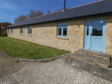 A stone building with blue doors and windows surrounded by a lawn and gravel at Stapleford Farm in Hooke near Beaminster