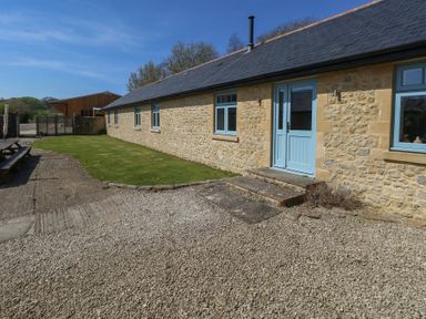 A stone exterior wall with blue windows and door next to a gravel area and grass at Stapleford Farm in Hooke near Beaminster
