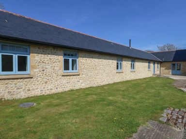 A stone exterior wall with blue framed windows and a slate roof beside a lawn at Stapleford Farm in Hooke near Beaminster