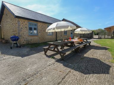 An outdoor patio area with wooden picnic tables and umbrellas beside a stone building at Stapleford Farm in Hooke near Beaminster