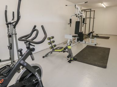 A home gym with exercise bike, weight machine, ab bench, mats, and weights at Stapleford Farm in Hooke near Beaminster