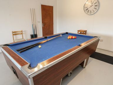 A room with a pool table, pool cues, a chair, a small table and a wall clock at Stapleford Farm in Hooke near Beaminster