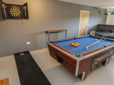 A game room with a pool table set for play a dartboard on the wall a narrow table and a ping pong table in the background at Stapleford Farm in Hooke near Beaminster