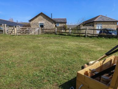 A grassy yard with wooden fences and stone buildings in the background and a wooden box with croquet mallets in the foreground at Stapleford Farm in Hooke near Beaminster