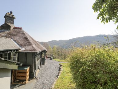 A gravel path beside a house with a slate roof and a green bush with hills in the background at Bwthyn y Coediwr in Tan Y Bwlch Maentwrog
