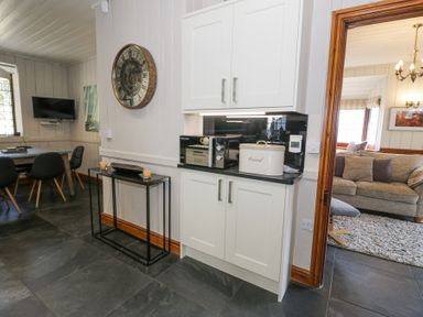 A kitchen with white cabinets a microwave and breadbin next to a dining area and living room at Bwthyn y Coediwr The Woodcutters Cottage in Tan Y Bwlch Maentwrog