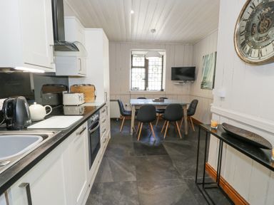 A kitchen with a dining table and chairs and a wall clock at Bwthyn y Coediwr The Woodcutters Cottage in Tan Y Bwlch Maentwrog