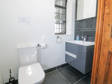 A bathroom with a toilet paper holder a sink cabinet and a window at Bwthyn y Coediwr The Woodcutters Cottage in Tan Y Bwlch Maentwrog