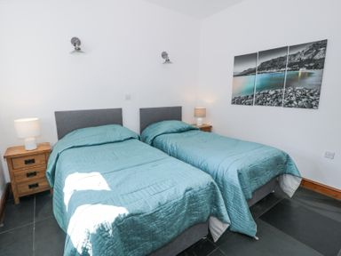 A bedroom with two single beds with teal bedspreads two wooden bedside tables with lamps and a three-panel wall picture at Bwthyn y Coediwr (The Woodcutters Cottage) in Tan Y Bwlch Maentwrog