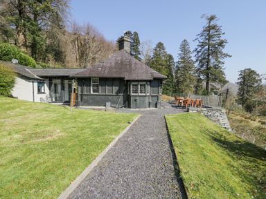 A cottage with slate roof and gravel pathway surrounded by grass and trees at Bwthyn y Coediwr in Tan Y Bwlch Maentwrog