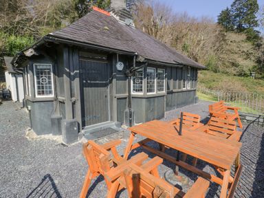 An outdoor patio with wooden table and chairs outside a dark wood cottage at Bwthyn y Coediwr The Woodcutters Cottage in Tan Y Bwlch Maentwrog