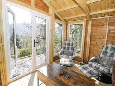 A wooden room with two plaid armchairs a wooden table and large glass doors at Bwthyn y Coediwr The Woodcutters Cottage in Tan Y Bwlch Maentwrog