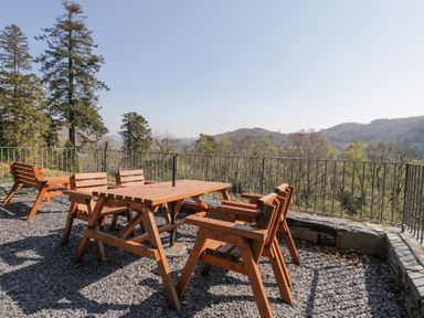An outdoor seating area with wooden table and chairs on a gravel terrace overlooking trees and hills at Bwthyn y Coediwr The Woodcutters Cottage in Tan Y Bwlch Maentwrog