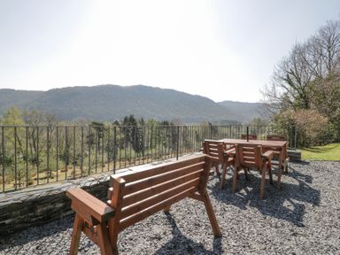 An outdoor seating area with wooden benches and chairs overlooking a forested hillside at Bwthyn y Coediwr The Woodcutters Cottage in Tan Y Bwlch Maentwrog
