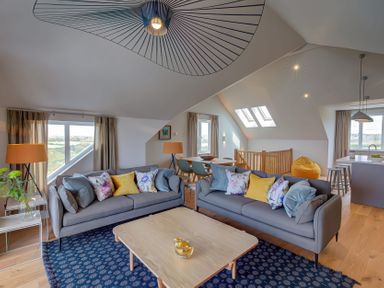 A living room with two sofas and cushions a coffee table and lamps with dining area and kitchen in the background at Villa 4 Mullion