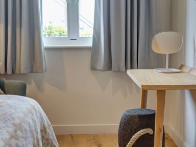 A bedroom corner with a window covered by curtains a wooden desk with a mirror on top and a textured stool below at Villa 4 Mullion
