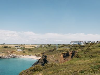 A coastal landscape with cliffs, a small beach, and buildings including a large white building at Villa 4 in Mullion