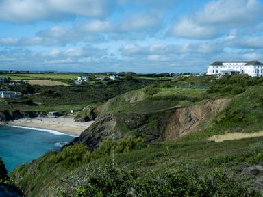 A coastal landscape with cliffs a sandy beach houses and a large white building on a hill at Villa 5 in Mullion