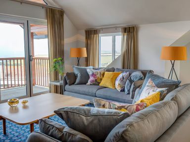 A living room with sofas, cushions, lamps, a coffee table, and sliding balcony doors at Villa 6 Mullion