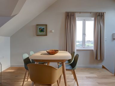 A dining area with a wooden table and five chairs near a window with curtains at Villa 6 in Mullion
