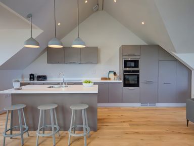 A kitchen with stools at a counter and cabinets with appliances at Villa 6 in Mullion
