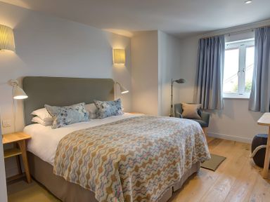 A bedroom with a bed covered with patterned blankets and pillows a chair near a window with curtains and wooden flooring at Villa 6 in Mullion