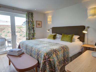 A bedroom with a bed with green pillows and a patterned blanket two bedside tables and a bench with towels at Villa 6 in Mullion