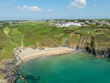 A coastal landscape with a sandy beach surrounded by cliffs and green fields with buildings in the background at Villa 6 in Mullion