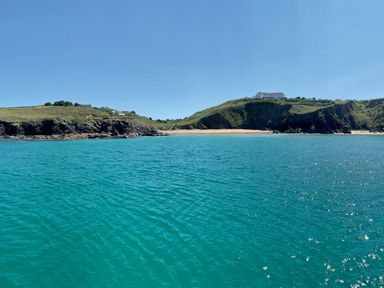 A coastal landscape with a sandy beach between two grassy hills and clear blue water at Villa 6 Mullion