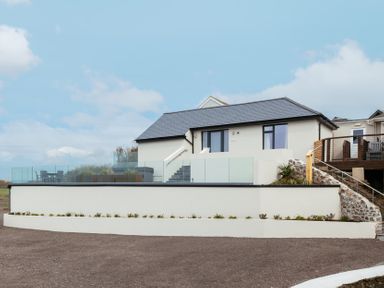 A modern white house with a slate roof glass balcony and outdoor seating at Shearwater in Mullion