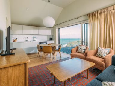 A living room with a wooden table orange chairs and a large sliding door opening to a sea view at Shearwater in Mullion
