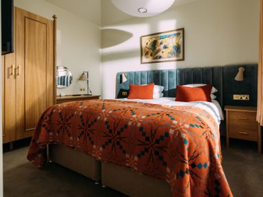 A bedroom with a bed covered by an orange patterned blanket and two orange pillows at Shearwater in Mullion