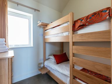 A bedroom with wooden bunk beds a small wooden cabinet with folded towels and a window at Shearwater Mullion