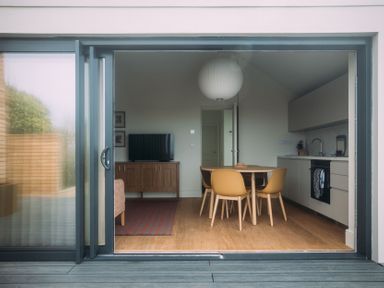 A kitchen and dining area with a round table and four chairs and a television on a wooden cabinet at Shearwater in Mullion