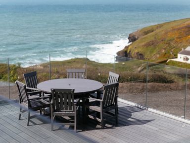 An outdoor patio with a round table and six chairs overlooking the sea and cliffs at Shearwater in Mullion