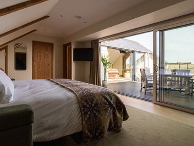 A bedroom with a bed and doors leading to a deck at Trevean in Mullion