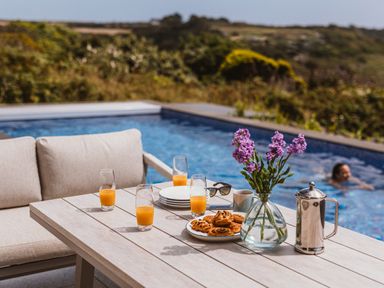 An outdoor table with drinks and snacks by a swimming pool at Trevean in Mullion