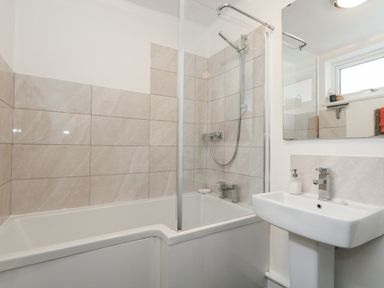 A bathroom featuring a bathtub with shower and a sink at Fisherman’s Cottage