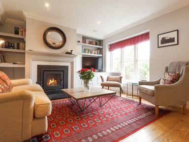 A living room with a fireplace two armchairs a sofa a coffee table with flowers and built in bookshelves at Sea Crest in Aldeburgh