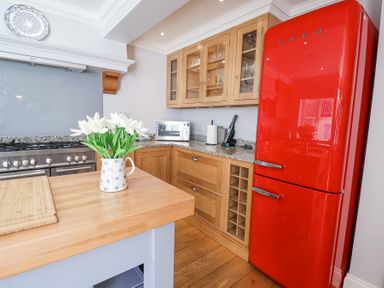 A kitchen with a red fridge wooden cabinets a microwave and flowers on a countertop at Sea Crest in Aldeburgh