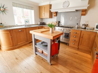 A kitchen with wooden cabinets a countertop island with flowers and kitchen appliances at Sea Crest in Aldeburgh