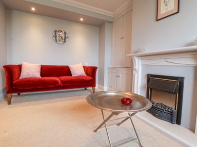 A living room with a red sofa white cushions a metal tray table and a fireplace at Sea Crest in Aldeburgh