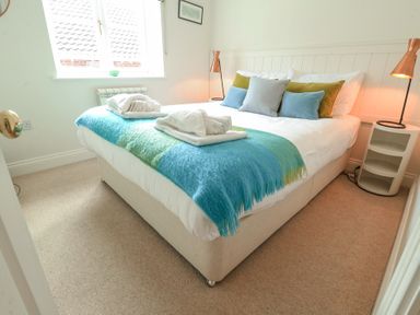 A bedroom with a bed with blue and green throw and pillows with bedside tables and lamps at Sea Crest in Aldeburgh