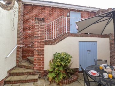 A patio with brick walls and steps a round planter with plants a metal table with cups and an umbrella at Sea Crest in Aldeburgh