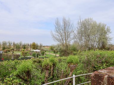 An outdoor scene with trimmed bushes trees and a pathway with fields in the background at Sea Crest in Aldeburgh