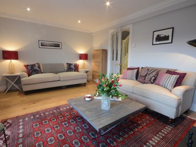 A living room with two beige sofas a wooden coffee table with flowers and a red patterned rug at Sea Crest Aldeburgh